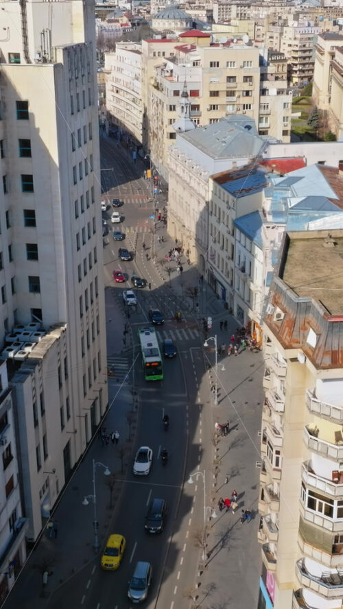 Video - Vertical aerial drone view of a downtown road with moving traffic and walking people. Sunny day in Bucharest, Romania
