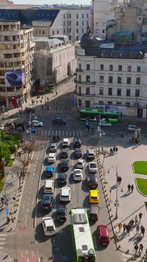 Video - Bucharest, Romania - March 03, 2024: Vertical aerial drone view of a downtown road with moving traffic and walking people. Sunny day