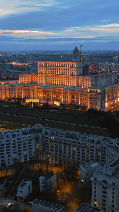Video - Vertical aerial drone view of illuminated Palace of the Parliament in Bucharest downtown in the evening. Multiple districts around. Romania