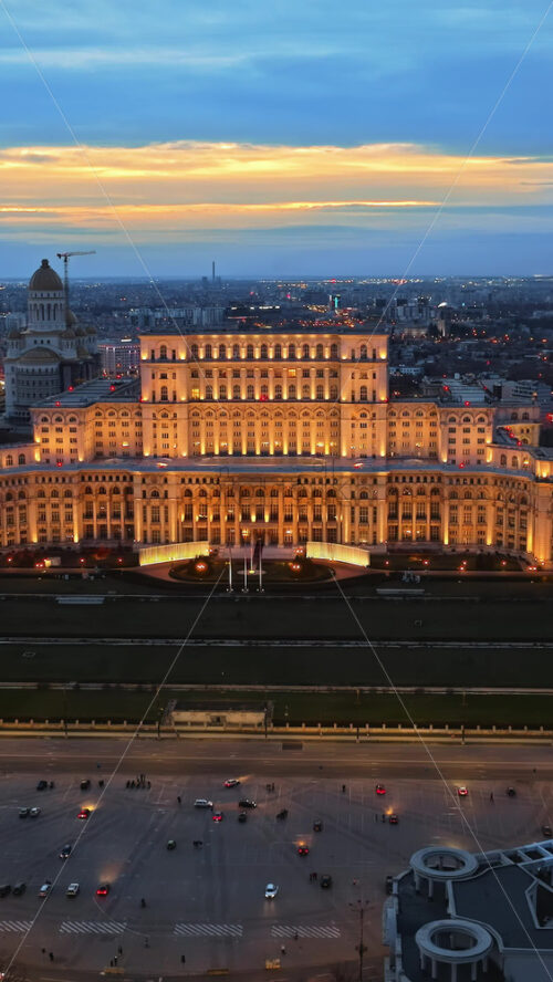 Video - Vertical aerial drone view of illuminated Palace of the Parliament in Bucharest downtown in the evening. Multiple districts around. Romania