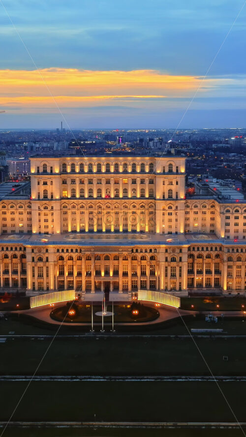 Video - Vertical aerial drone view of illuminated Palace of the Parliament in Bucharest downtown in the evening. Multiple districts around. Romania