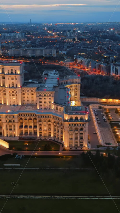 Video - Vertical aerial drone view of illuminated Palace of the Parliament in Bucharest downtown in the evening. Multiple districts around. Romania