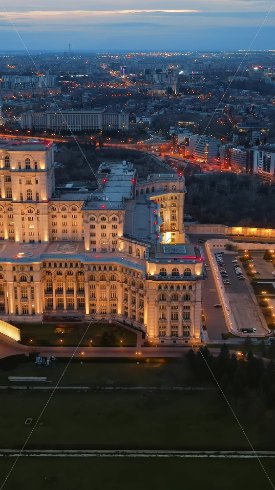 Video - Vertical aerial drone view of illuminated Palace of the Parliament in Bucharest downtown in the evening. Multiple districts around. Romania