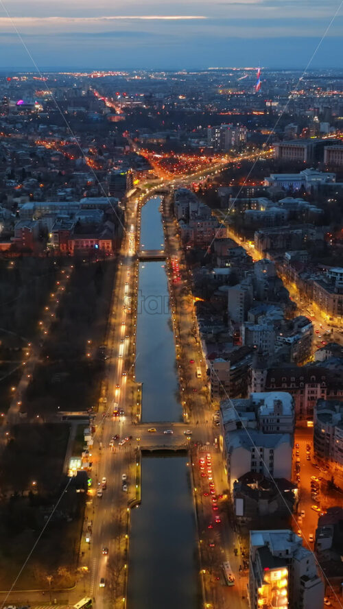 Video - Vertical aerial drone view of the illuminated city in the evening. Moving traffic. Blue hour in Bucharest, Romania