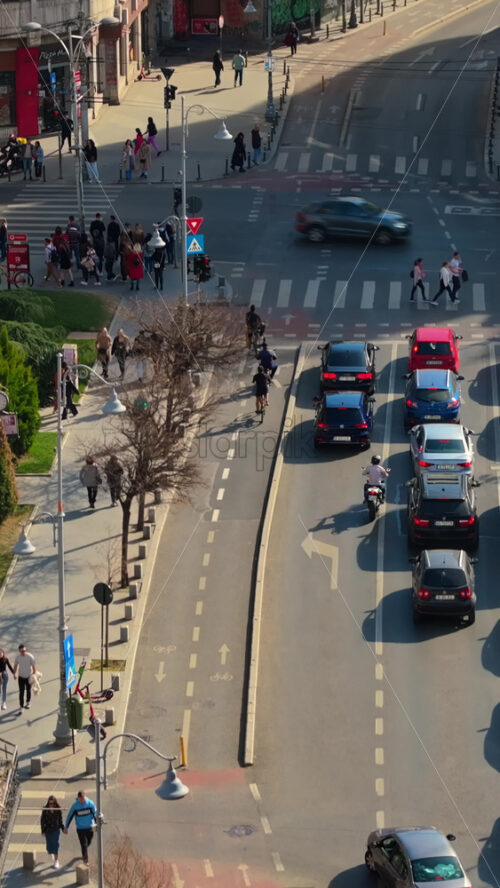 Video - Bucharest, Romania - March 03, 2024: Vertical aerial drone view of a downtown road with moving traffic and walking people. Sunny day