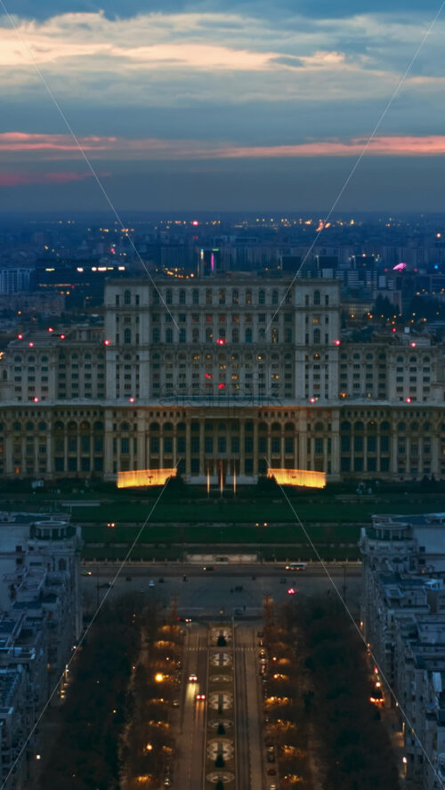 Video - Vertical aerial hyperlpase timelapse drone view of illuminated Palace of the Parliament in Bucharest downtown in the evening. Multiple districts around. Romania