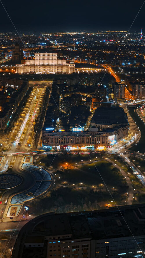 Video - Vertical aerial hyperlapse timelapse drone view of illuminated Palace of the Parliament in city downtown in the night. Multiple districts around