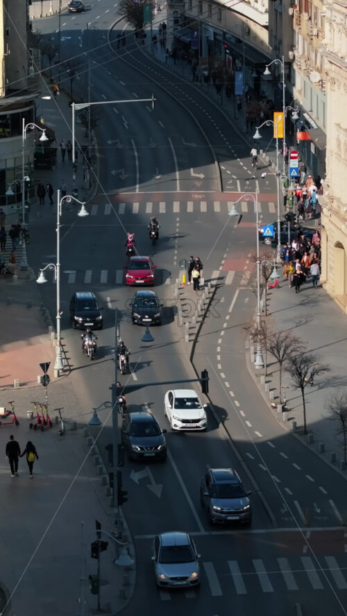 Video - Bucharest, Romania - March 03, 2024: Vertical aerial drone view of a downtown road with moving traffic and walking people. Sunny day