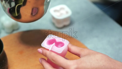 Video - A woman occupied with hand made candles production, pouring melted wax into the mold. Slow motion