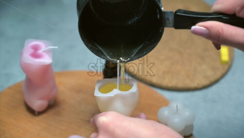 Video - A woman occupied with hand made candles production, pouring melted wax into the mold. Slow motion