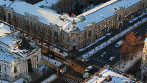 Video - Aerial drone view of Chisinau City Hall at sunset. Ground covered in snow. Moving traffic. Moldova