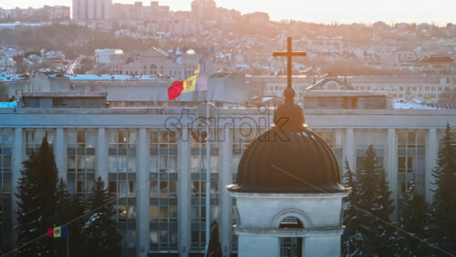 Video - Aerial drone view of Moldova national flag and the Government House at sunset. Golden crosses on top of the Bell tower and the Metropolitan Cathedral of Christ's Nativity in foreground. Snowy Chisinau