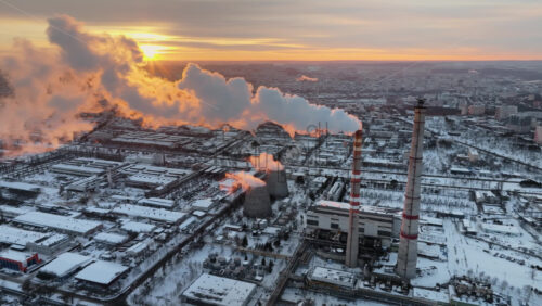 Video - Aerial drone view of a working thermal power station in Chisinau at sunset. City covered in snow. Steam and smoke coming from pipes. Moldova
