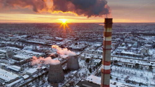 Video - Aerial drone view of a working thermal power station in Chisinau at sunset. City covered in snow. Steam and smoke coming from pipes. Moldova