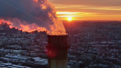 Video - Aerial drone view of a working thermal power station in Chisinau at sunset. City covered in snow. Steam and smoke coming from pipes. Moldova