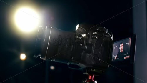 Video - Young content creator talking and gesturing man turning on the camera on a tripod and recording a vlog. Working from home