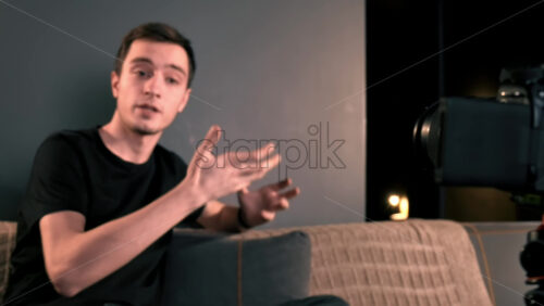 Video - Young content creator talking and gesturing, using a camera on a tripod while recording a vlog. Working from home