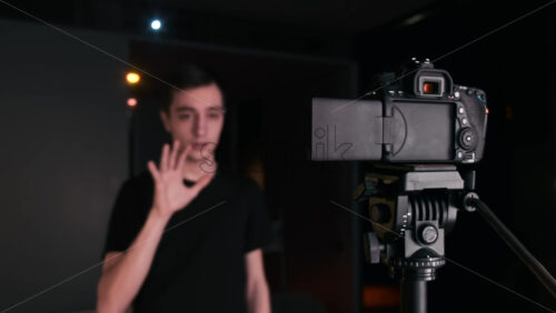 Video - Young content creator talking and gesturing man filming himself using a camera on a tripod while recording a vlog. Working from home