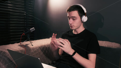 Video - Young content creator talking and gesturing man is on his laptop sitting on the sofa. Working from home