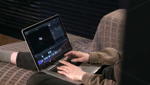 Video - Young content creator girl is on her laptop sitting on the sofa. Working with video from home