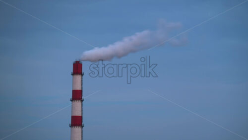 Video - Timelapse of a red and white smokestack emitting a plume of smoke into the air with the evening sky on the background