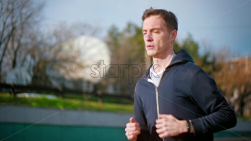 Video - Young focused man running in jacket. Moving cars. Cloudy weather. Slow motion