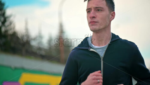 Video - Young focused man running in jacket. Cloudy weather. Slow motion