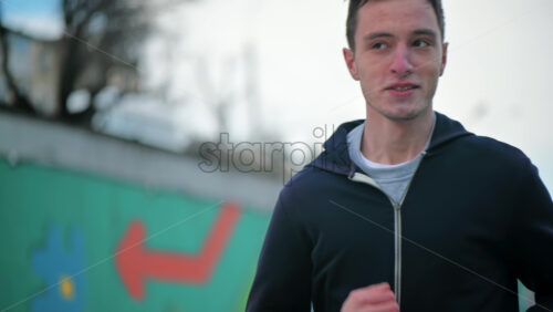 Video - Young focused man running in jacket. Cloudy weather. Slow motion