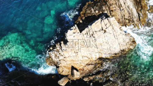 Video - Aerial drone view of the Aegean sea rocky coast with rocks in the blue transparent water, waves and foam, top view, Greece