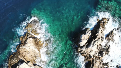 Video - Aerial drone view of the Aegean sea rocky coast with rocks in the blue transparent water, waves and foam, top view, Greece