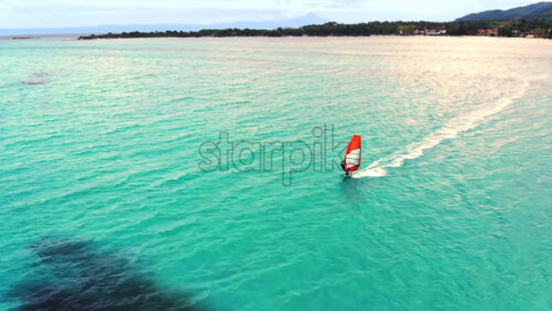 Video - Aerial drone view of a man at windsurfing in Aegean sea. Transparent water, land with greenery in Greece