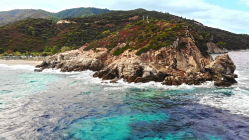 Video - Aerial drone view of the Aegean sea coast with camping near the beach, multiple greenery, hills on the background, blue water with waves. Greece