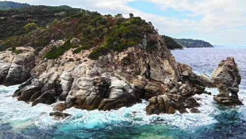 Video - Aerial drone view of the Aegean sea coast, multiple greenery, hills on the background, blue water with waves. Greece