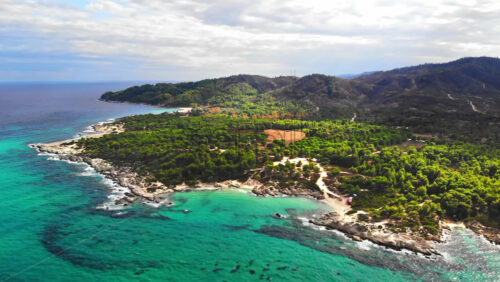 Video - Aerial drone view of the Aegean sea rocky coast with blue transparent water, multiple greenery, hills. Greece
