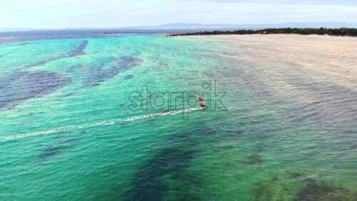 Video - Aerial drone view of a man at windsurfing in Aegean sea. Transparent water, land with greenery in Greece