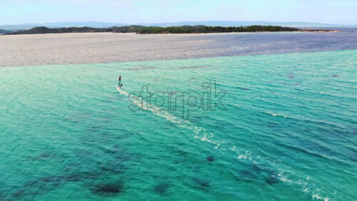 Video - Aerial drone view of a man at windsurfing in Aegean sea. Transparent water, land with greenery in Greece
