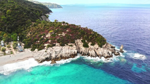 Video - Aerial drone view of the Aegean sea coast with camping near the beach, multiple greenery, hills on the background, blue water with waves. Greece