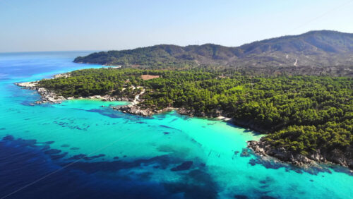 Video - Aerial drone view of the Aegean sea rocky coast with blue transparent water, multiple greenery, hills. Greece