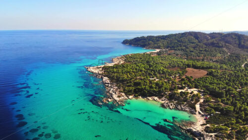 Video - Aerial drone view of the Aegean sea rocky coast with blue transparent water, multiple greenery, hills. Greece