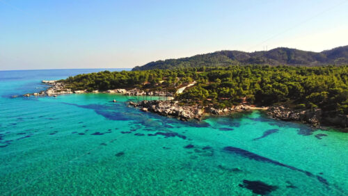 Video - Aerial drone view of the Aegean sea rocky coast with blue transparent water, multiple greenery, hills. Greece