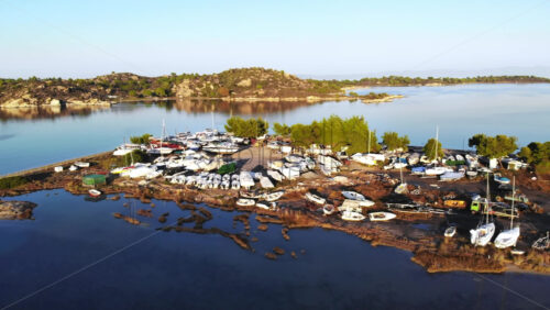 Video - Aerial drone view of an island in Aegean sea with multiple beached yachts and boats, rocks, greenery around, sunset, Greece