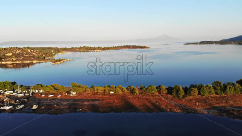 Video - Aerial drone view of an island in Aegean sea with multiple beached yachts and boats, rocks, greenery around, sunset, Greece