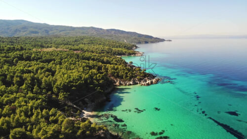 Video - Aerial drone view of the Aegean sea rocky coast with blue transparent water, multiple greenery, hills. Greece