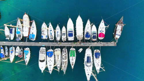 Video - Aerial drone view of Aegean sea port with multiple moored yachts at piers, blue water, top view, Greece