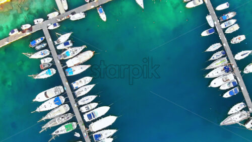 Video - Aerial drone view of Aegean sea port with multiple moored yachts at piers, blue water, top view, Greece