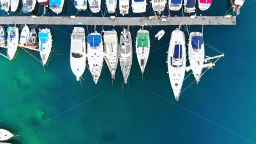 Video - Aerial drone view of Aegean sea port with multiple moored yachts at piers, blue water, top view, Greece