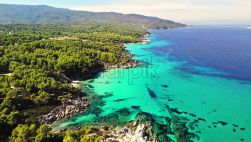 Video - Aerial drone view of the Aegean sea rocky coast with blue transparent water, multiple greenery, hills. Greece