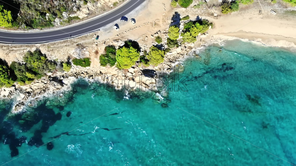 Video - Aerial drone view of the Aegean sea rocky coast with greenery and road along the shore, waves of the sea in Greece