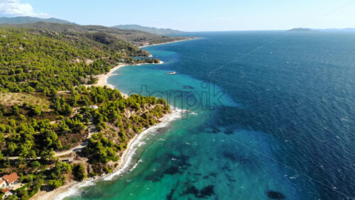 Video - Aerial drone view of the Aegean sea rocky coast with greenery and road along the shore, waves of the sea in Greece