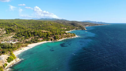 Video - Aerial drone view of the Aegean sea rocky coast with greenery, town and road along the shore, waves of the sea in Greece